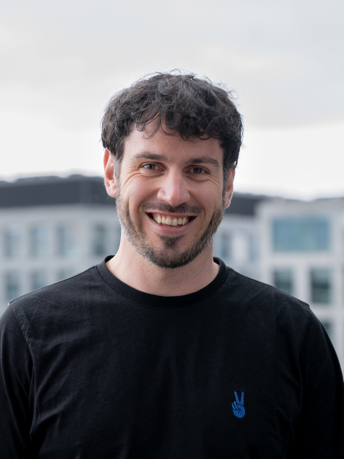 Lachendes Portrait eines Mitgründers der HUX Agency in schwarzem Shirt vor Bürogebäuden