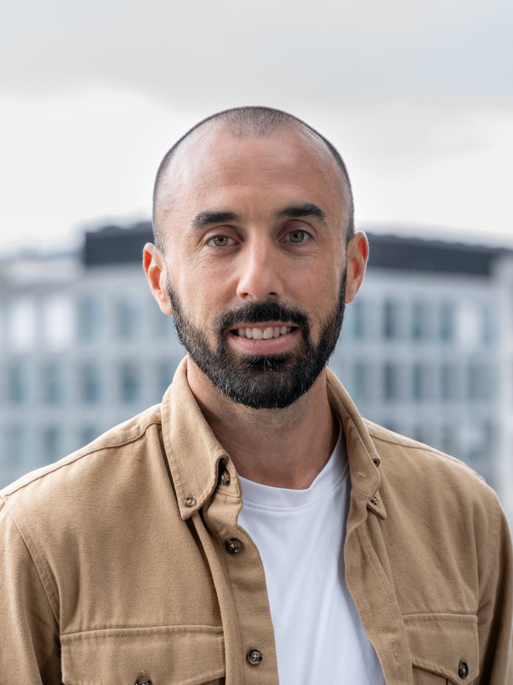 Portrait eines Mitgründers der HUX Agency in beigem Hemd vor Bürogebäuden