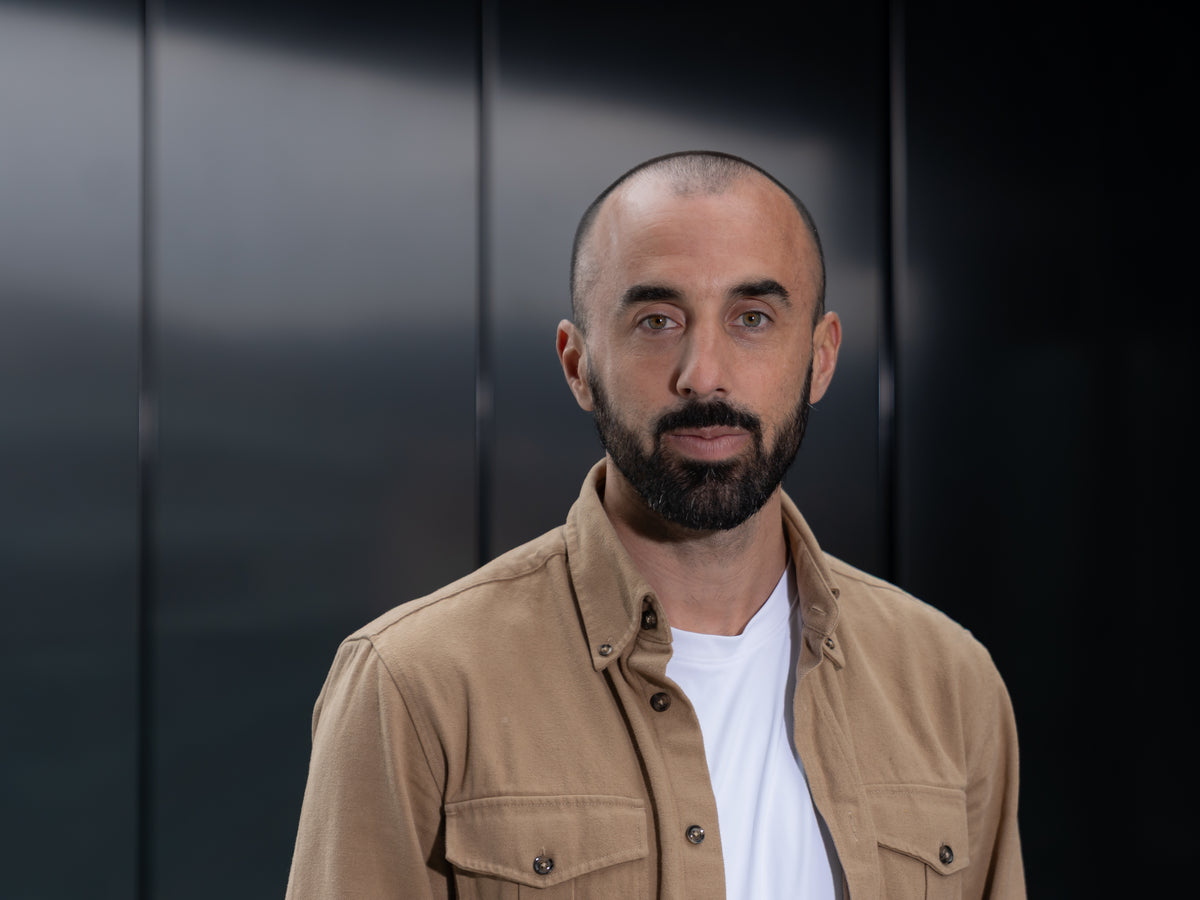 Portrait eines Mitgründers der HUX Agency in beigem Hemd vor dunklem Hintergrund